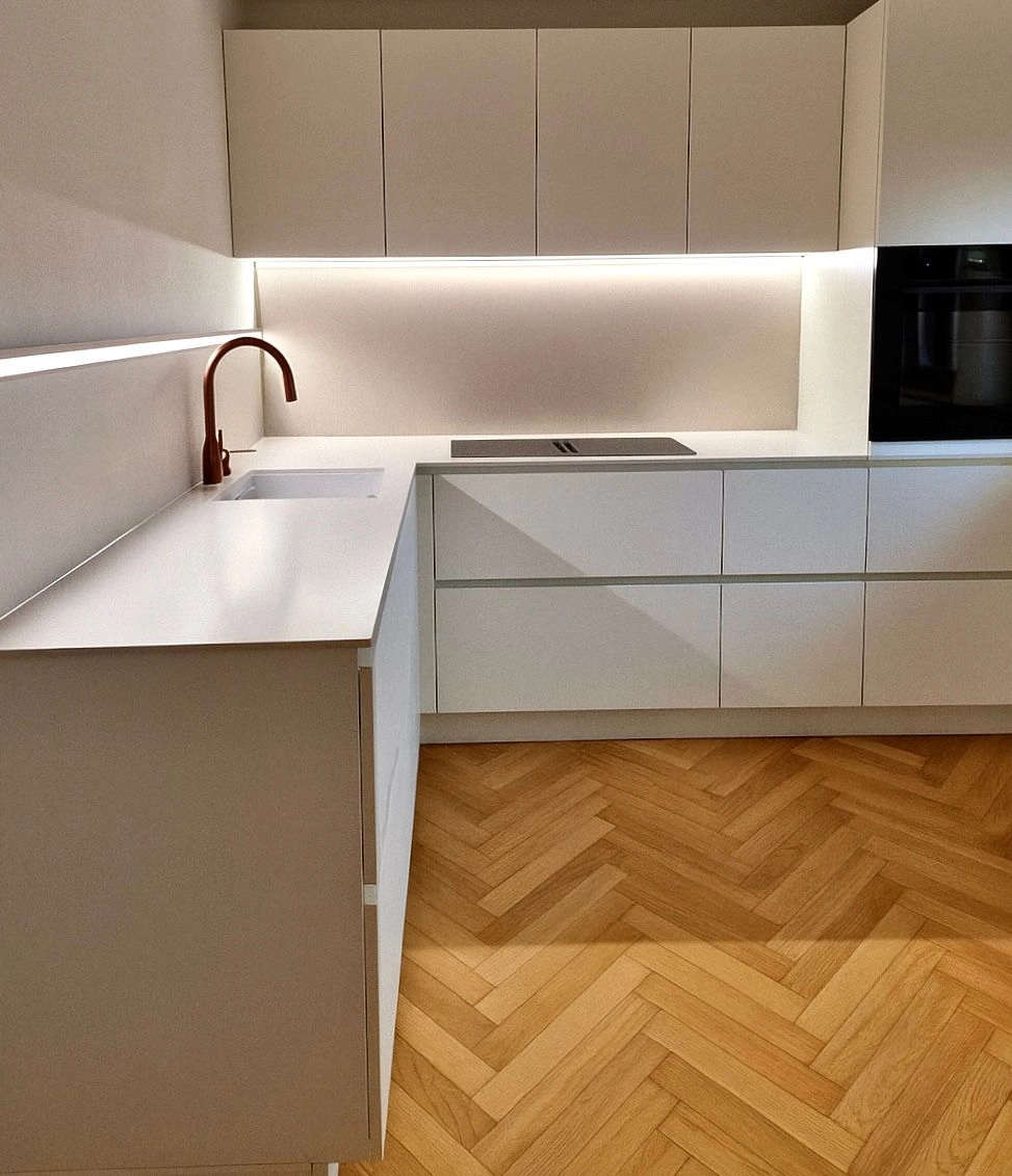 Moderne Einbauküche mit weißen Fronten, Holzfußboden und LED-Unterbauleuchte.