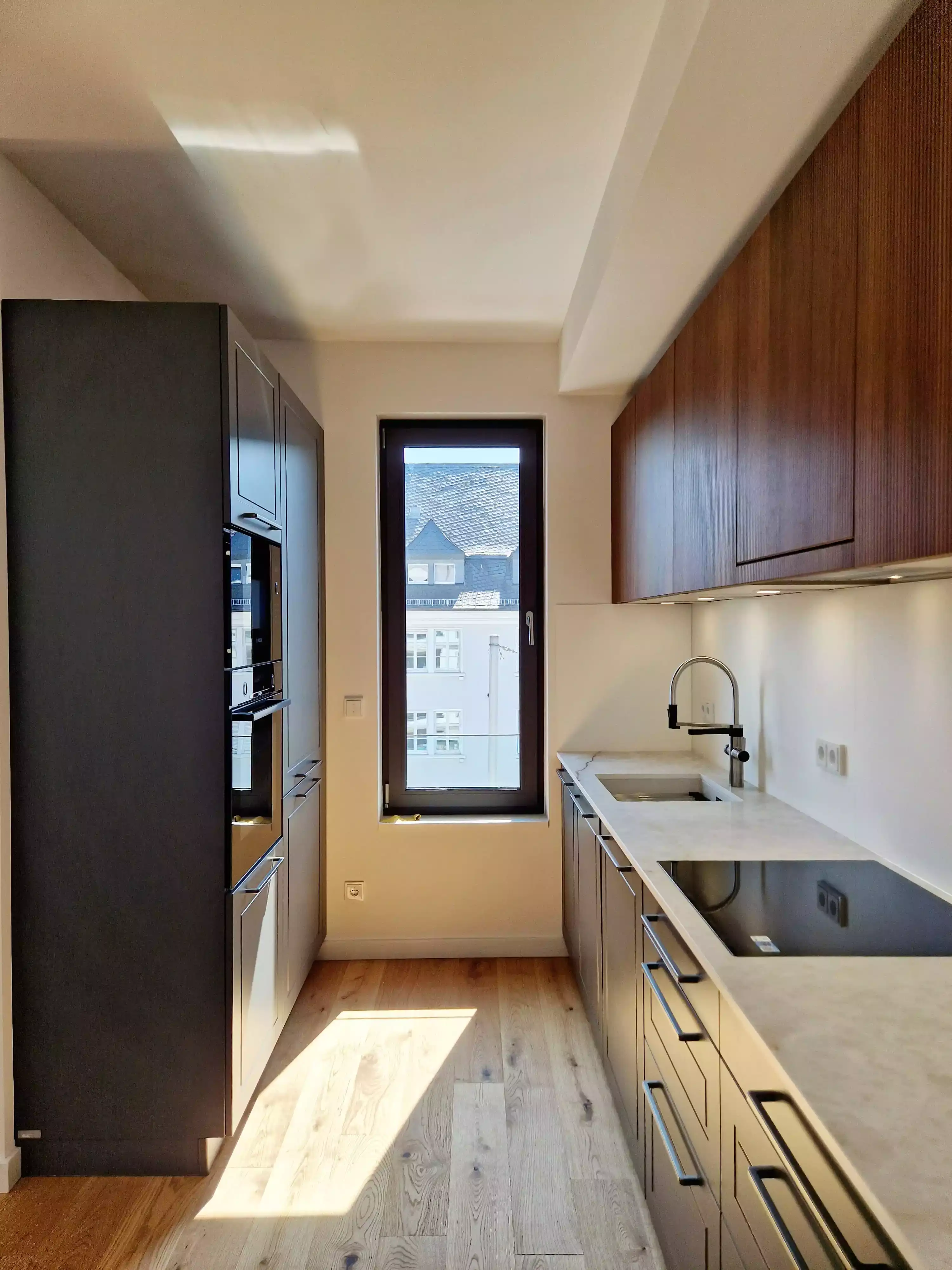 Moderne Einbauküche mit Holzfronten, Induktionskochfeld und großem Fenster mit Tageslicht.