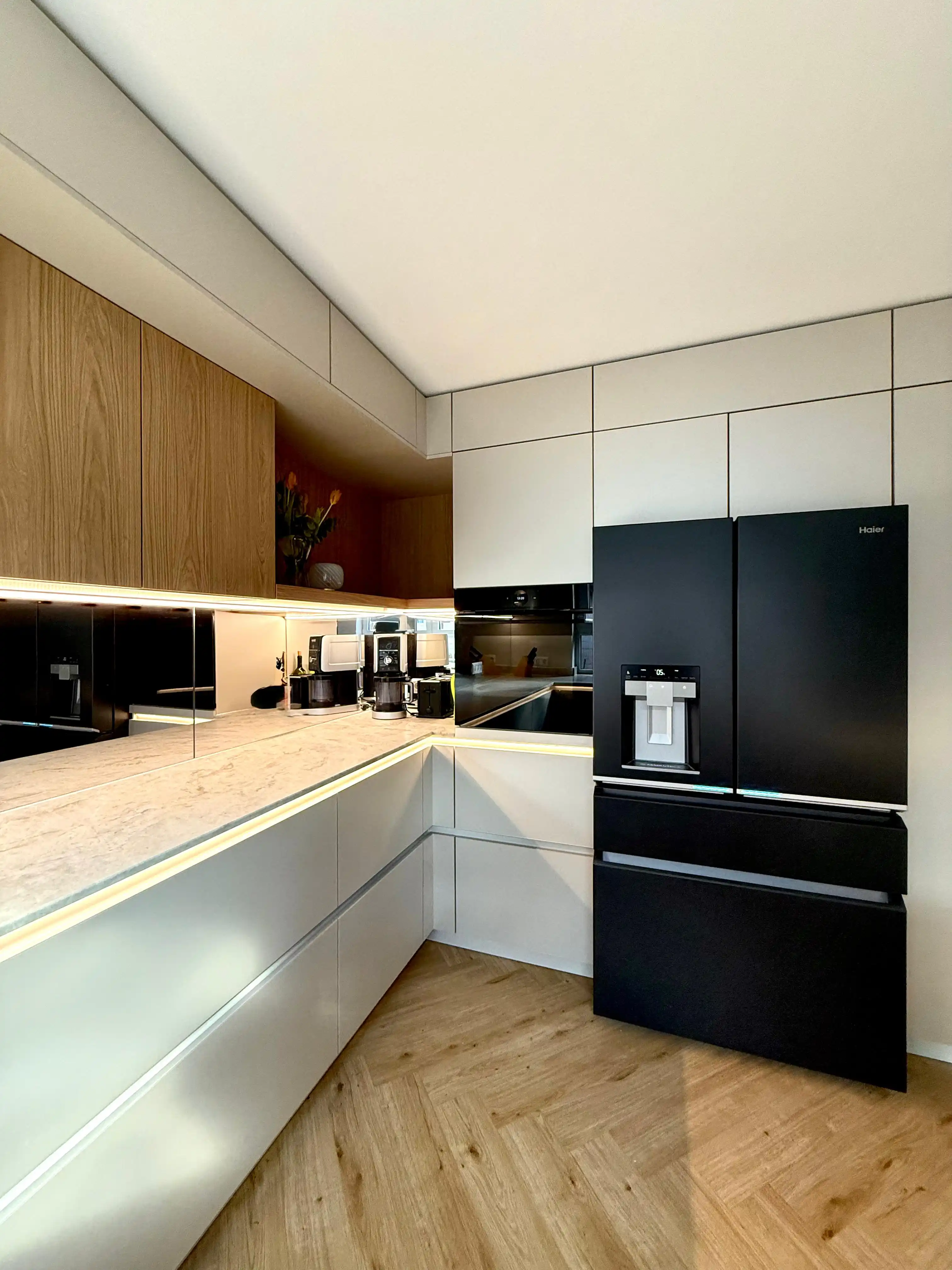 Moderne Einbauküche mit hellen Fronten, Holzdetails und schwarzem Kühlschrank.