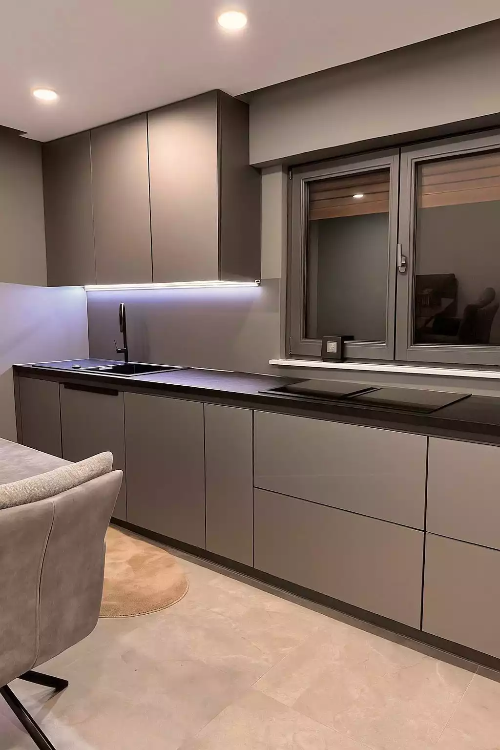 Moderne, minimalistische Einbauküche mit grauen Fronten, LED-Beleuchtung und Fenster.