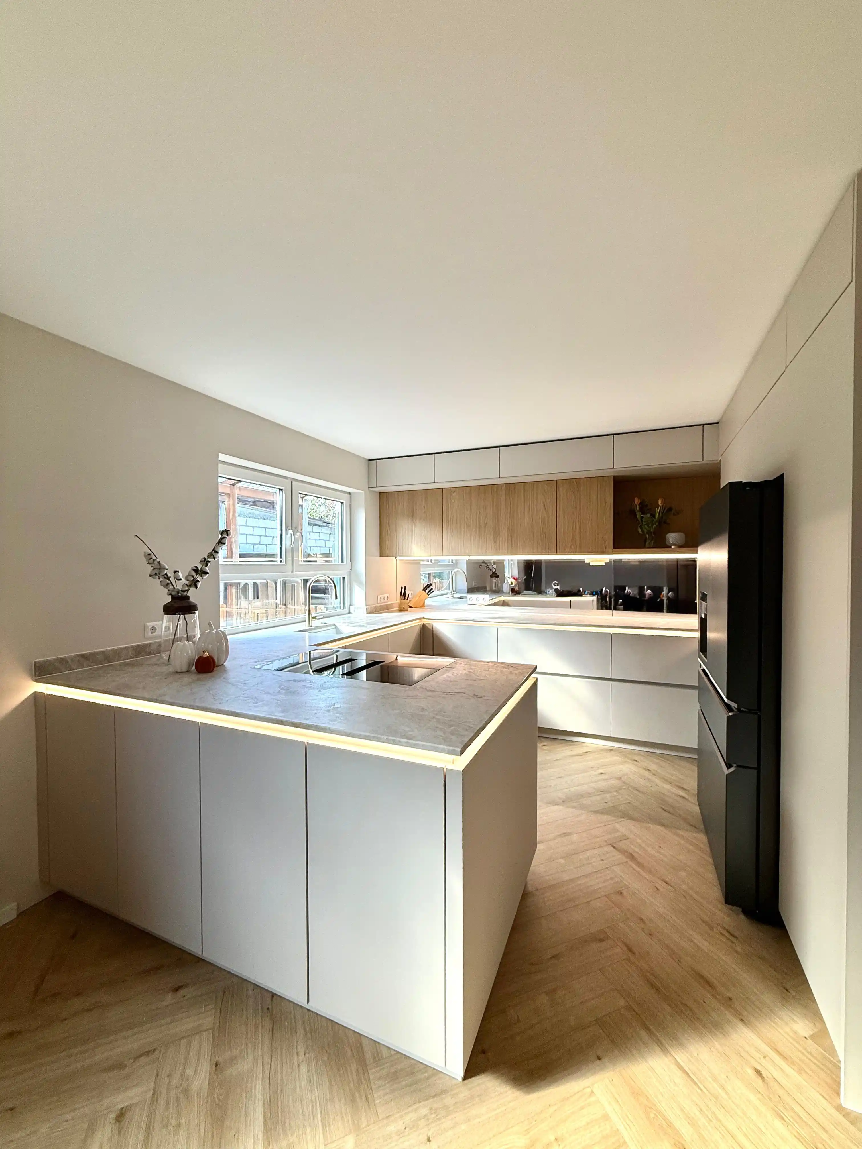 Moderne helle Einbauküche mit Kochinsel, Holzfronten und schwarzem Kühlschrank.